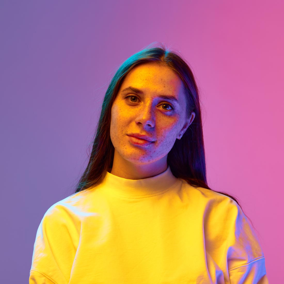 Close up portrait of young, beautiful, calm woman looking at camera against gradient purple pink background.